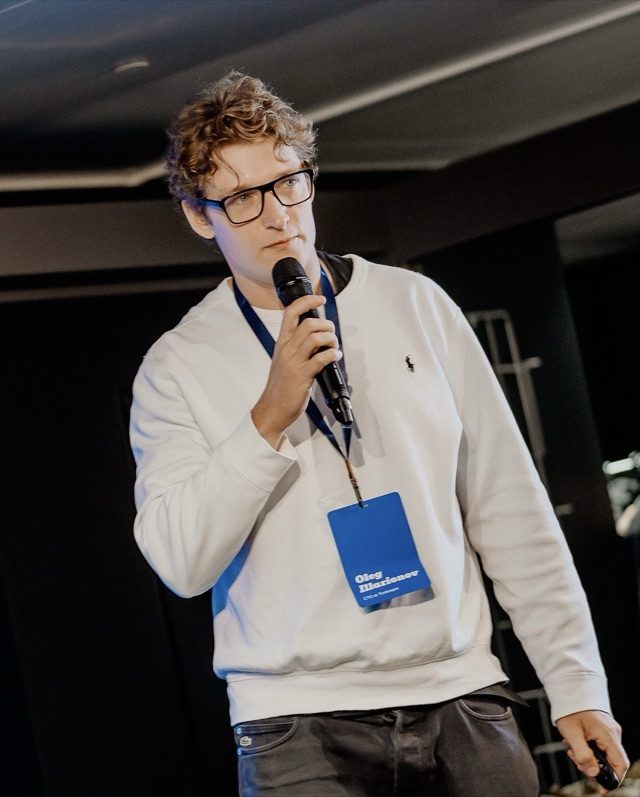 Oleg Illarionov speaking on stage, holding a microphone
